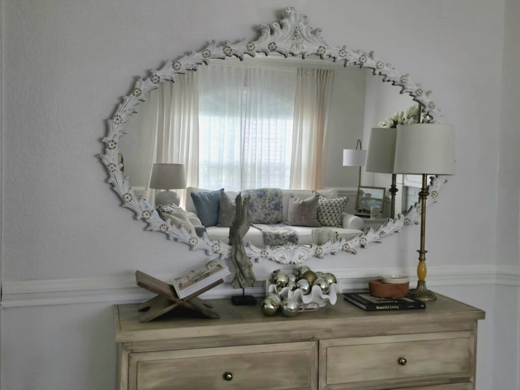 Carved white statement mirror reflecting a Soft Traditional living room with layered textiles and warm lighting.