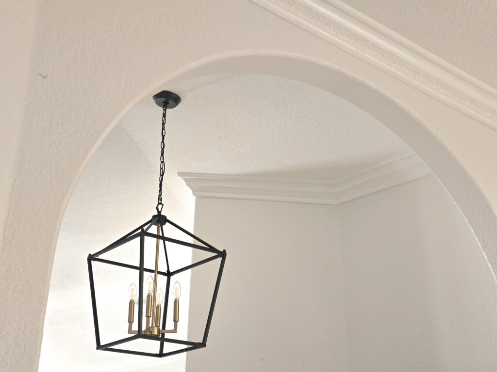 Black lantern chandelier hanging beneath an arched doorway with decorative crown molding.