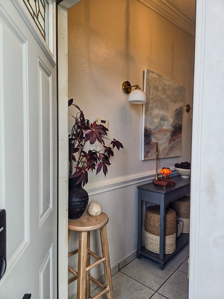 Entry foyer with open front door, large framed artwork, wood stool and neutral traditional decor.