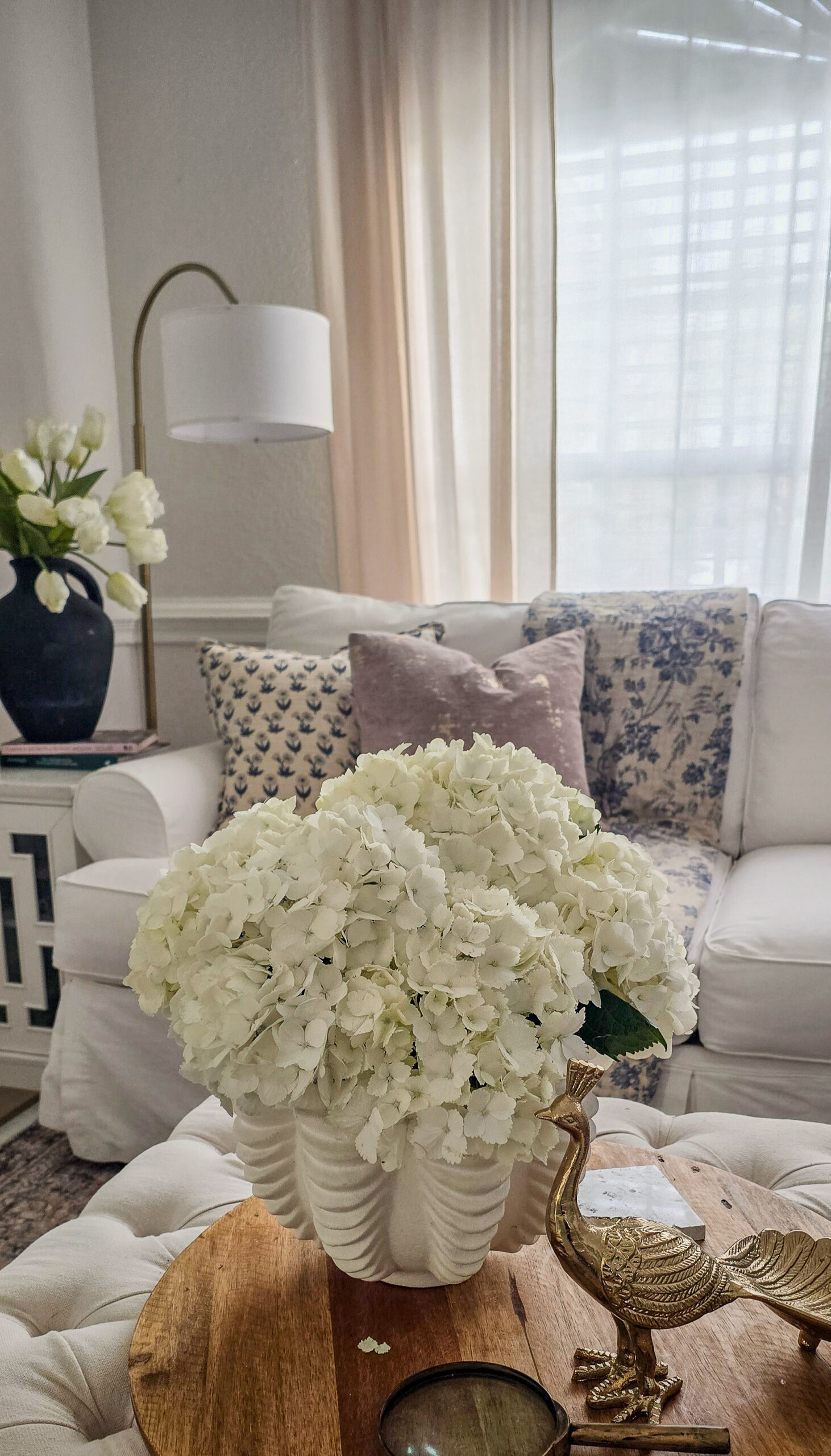 White hydrangeas arranged on a tray in a calm living room with natural textures and a neutral color palette.