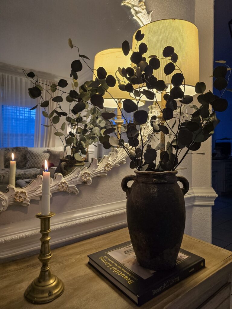 Eucalyptus branches in a rustic dark vase styled with an antique brass candlestick and warm lamplight