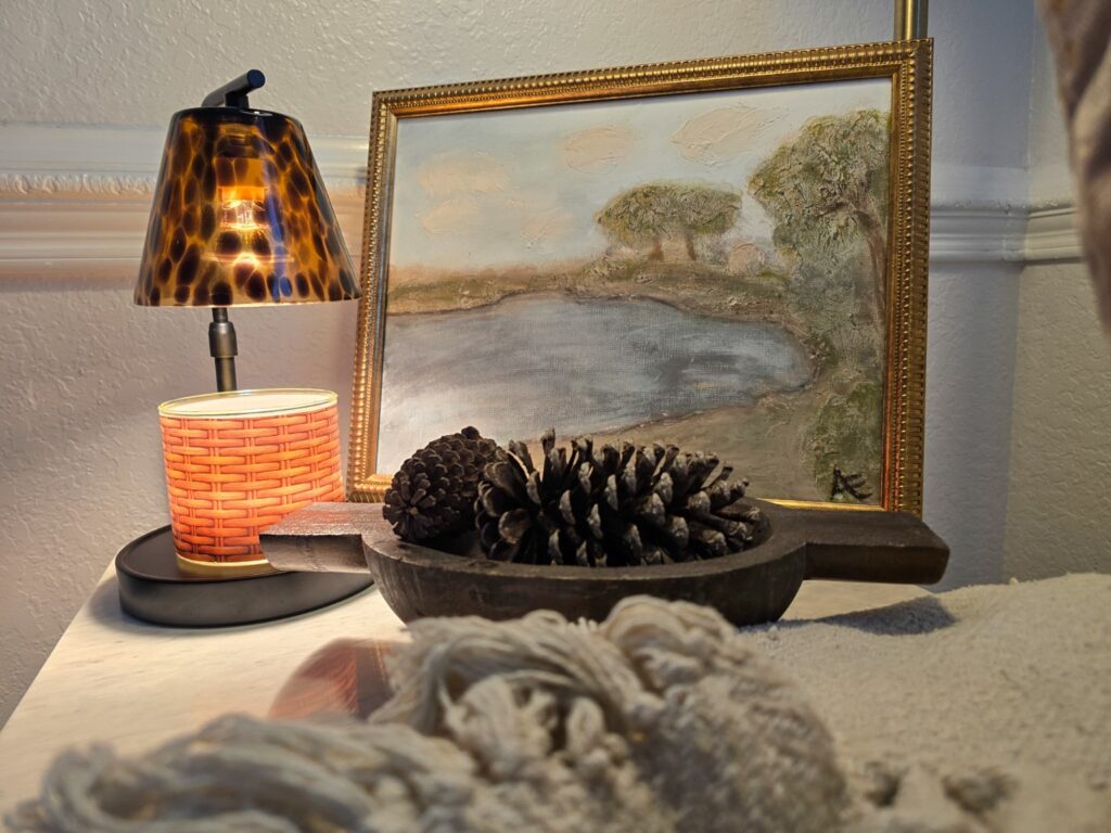 Warm fall vignette with tortoiseshell glass, pinecones, dark wood and a moody framed landscape