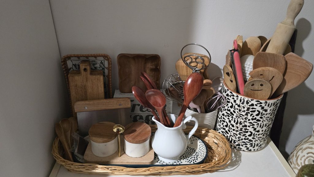 Open pantry shelves with pitcher, bowls, wooden spoons, and stacked wooden items.