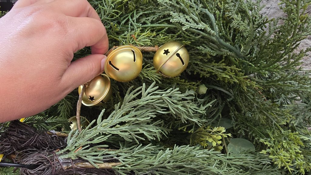 Hand selecting antique gold bells from evergreen Christmas greenery while