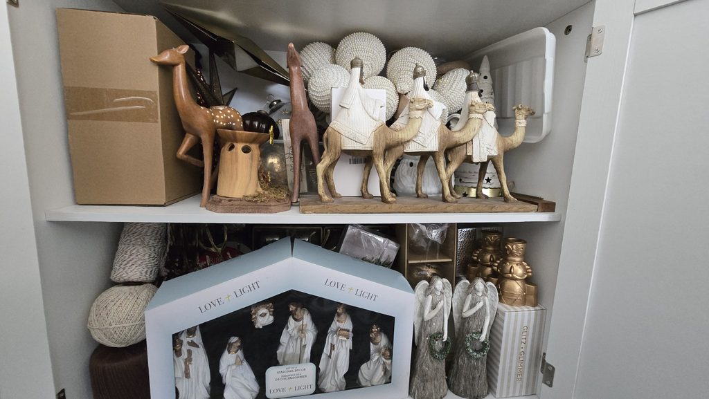 Christmas decorations stored in a cabinet, including nativity figures, angels, ornaments and seasonal decor.