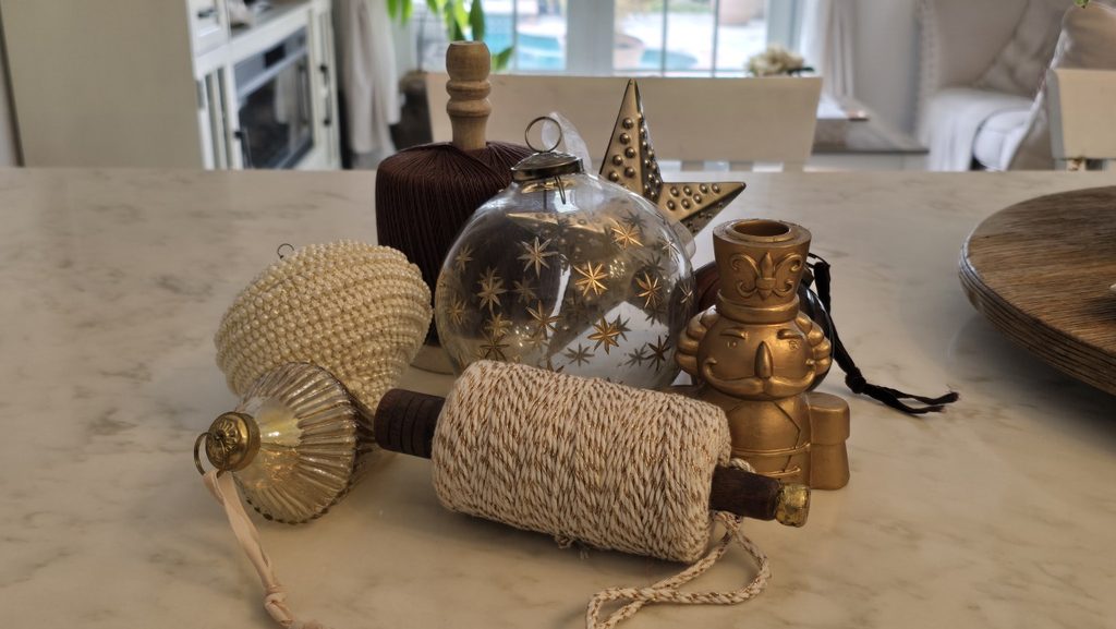 Christmas ornaments in antique gold, clear glass, cream and brown gathered together while planning Christmas decor.