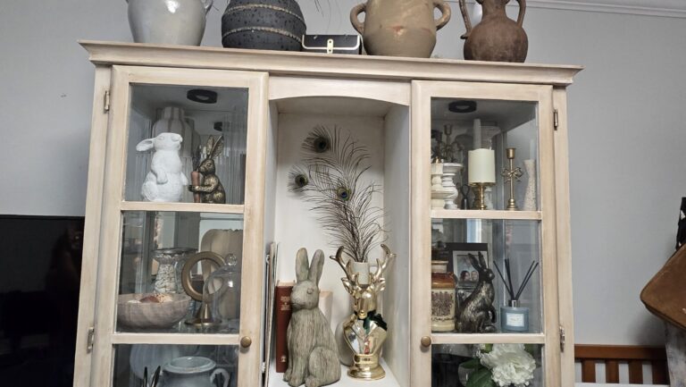Glass-front cabinet filled with collected home decor, pottery, glassware, and decorative objects.