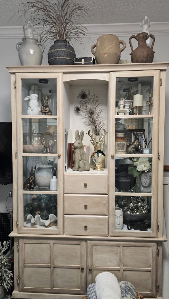 Full glass-front cabinet displaying collected pottery, vessels, candlesticks, and decorative objects.