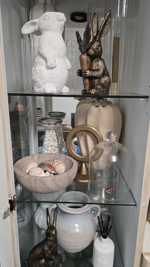 Glass cabinet shelves with collected rabbits, pottery, shells, glassware, and decorative objects.