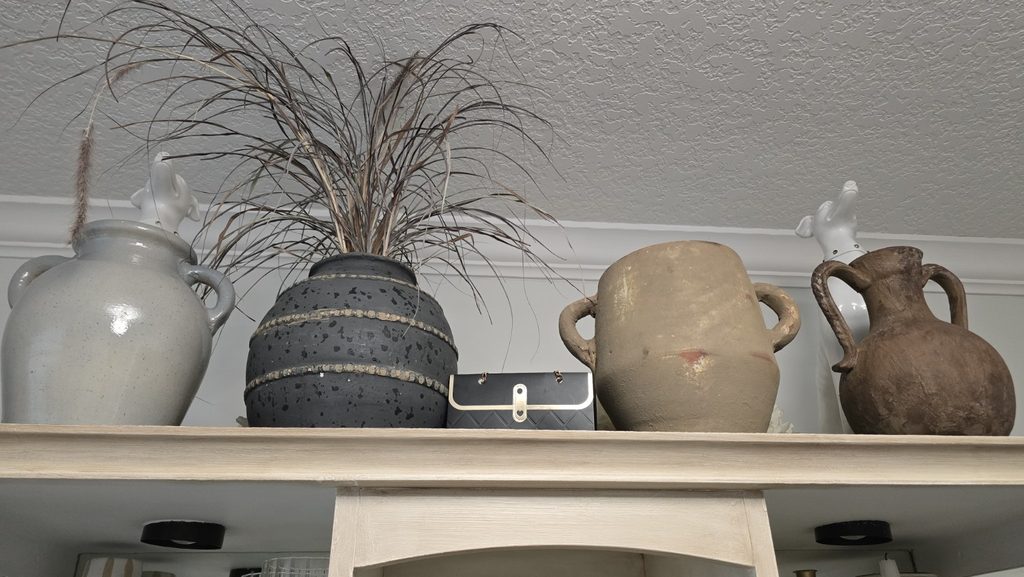 Collection of large ceramic and pottery vessels arranged on top of a glass-front cabinet.