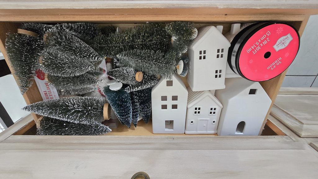White ceramic houses and green bottlebrush Christmas trees stored together in a drawer.
