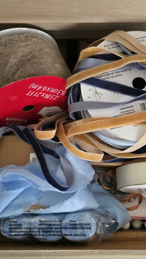 Christmas ribbon in dusty blue, navy, gold, cream and brown gathered in a drawer for decorating.
