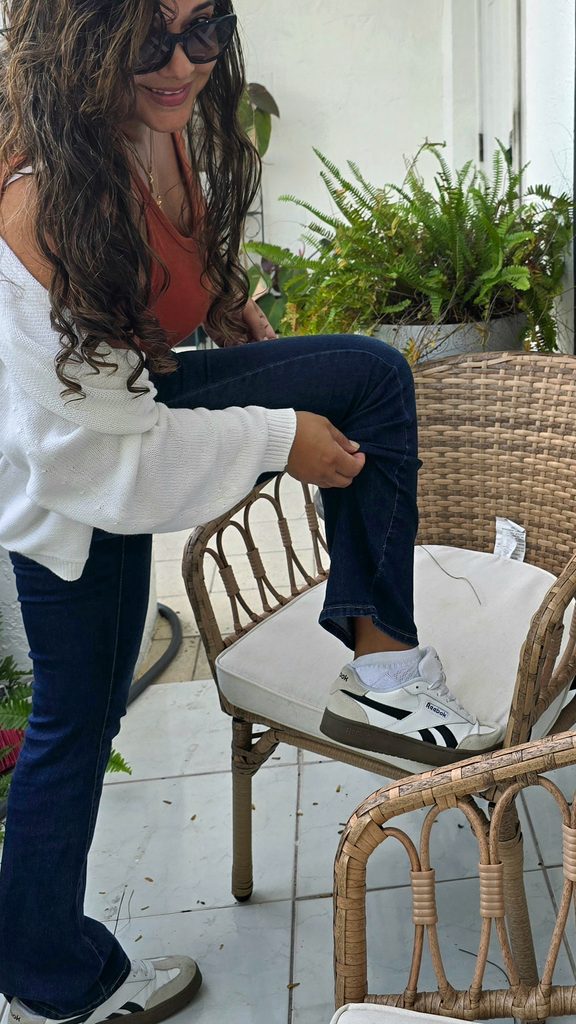 White cardigan layered over a rust tank with dark jeans and sneakers for casual fall style in Miami.