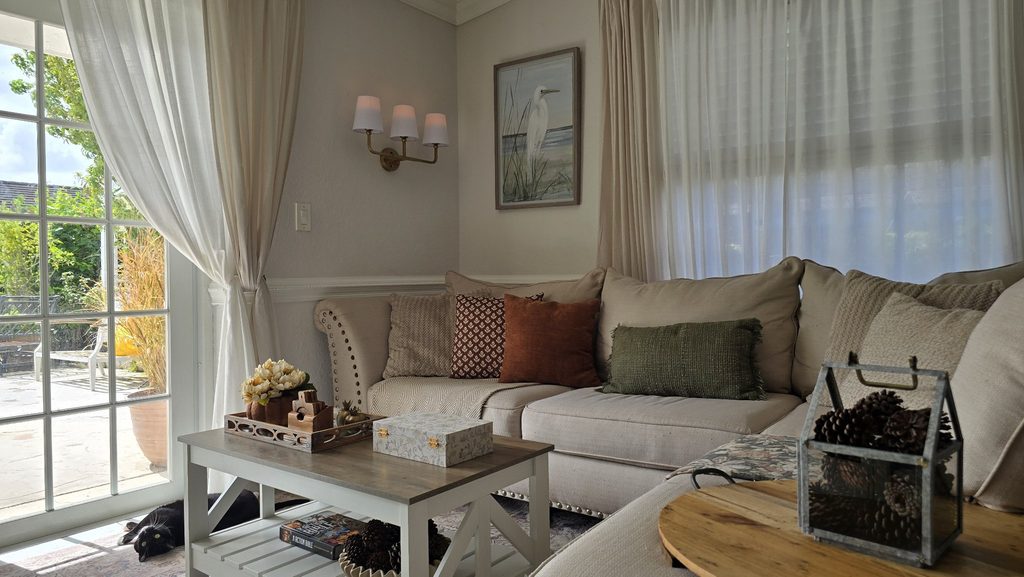 A wide view of a family room with French doors, a sofa with mixed pillows, a coffee table, and a pinecone lantern on a side table.