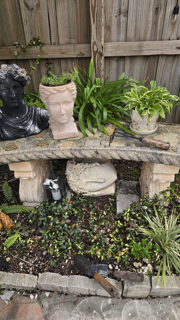 Bench with head busts and garden tools. 
