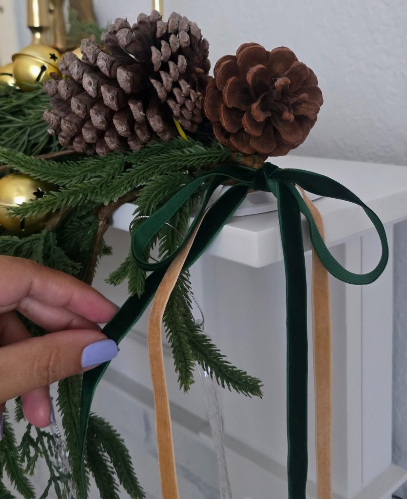 Thin green velvet floppy bow tied onto Christmas greenery with pinecones and ribbon tails