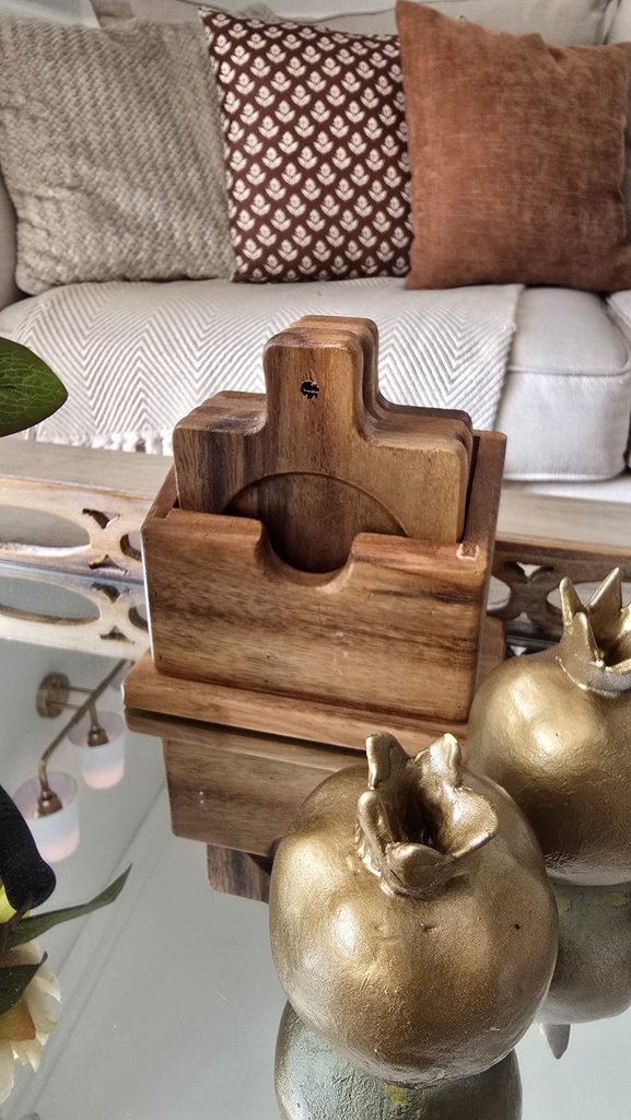 A mirrored tray holding gold pomegranate ornaments and a set of round wood coasters on a coffee table.